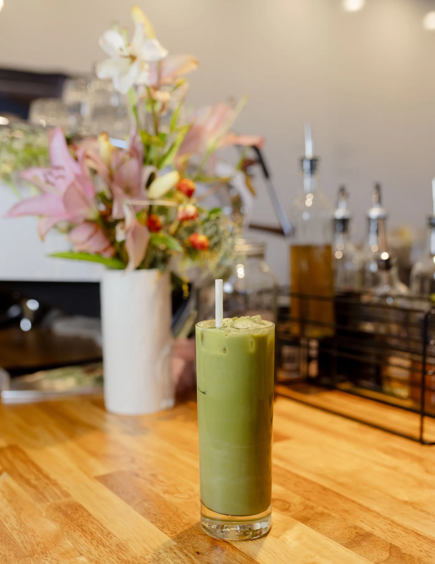 An iced matcha beside flowers on the coffee bar